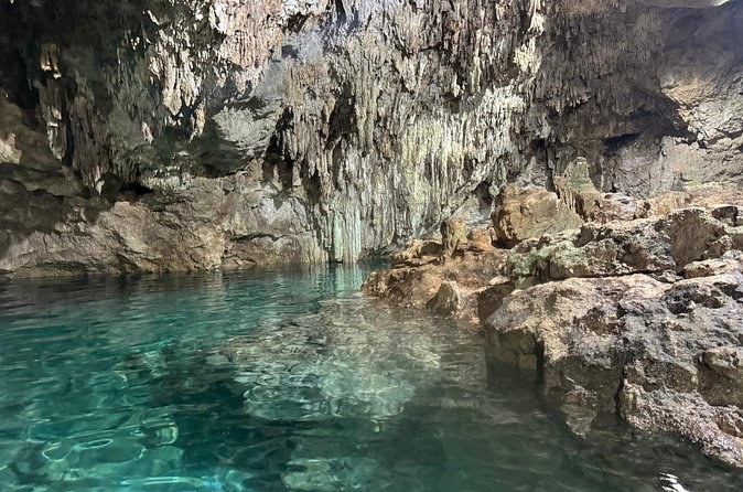 A cavern cenote with clear pale water running back under a low limestone roof