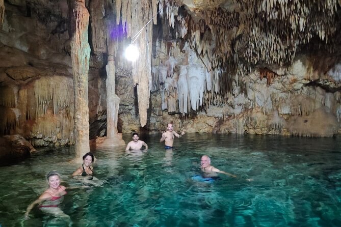 Swimmers in the shallow clear water of a cavern cenote under a roof of stalactites