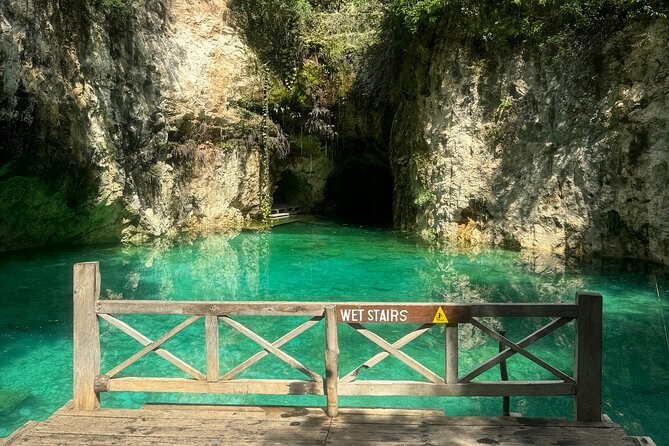 A wide open cenote with turquoise water and a timber stair at the entrance