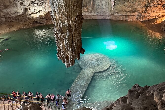 A cavern cenote with a stalactite column dropping to the water and a timber walkway around the edge