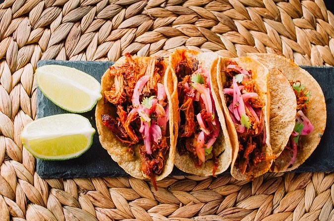 Three tacos of cochinita pibil topped with pickled red onion, with lime wedges alongside