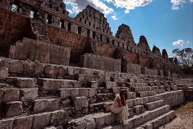 The stepped and carved stone facade of a building at Kabah with a visitor sitting on the lower course