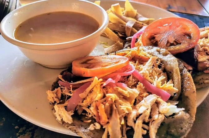 A plate of shredded meat with pickled onion and tomato beside a bowl of broth